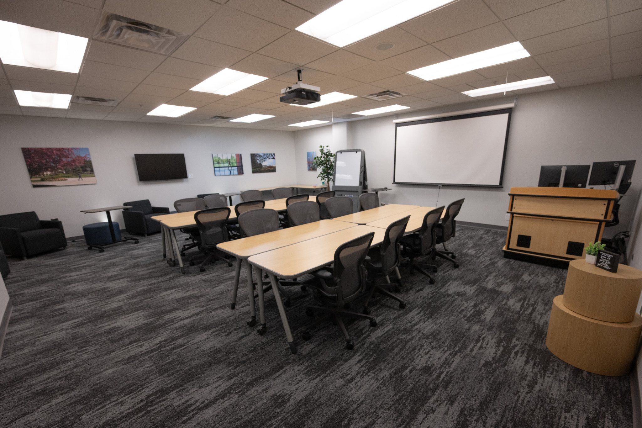 L243 instructional classroom with flexible tables, chairs, display screens, and projector
