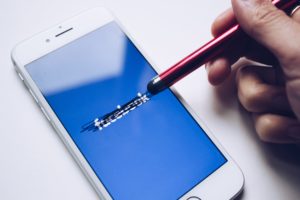 A person crossing out the Facebook logo on an iPhone screen with a stylus